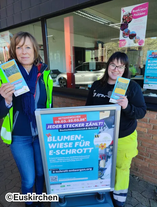 Zwei Frauen stehen vor einem Plakat der Aktion "Blumenwiese für E-Schrott"