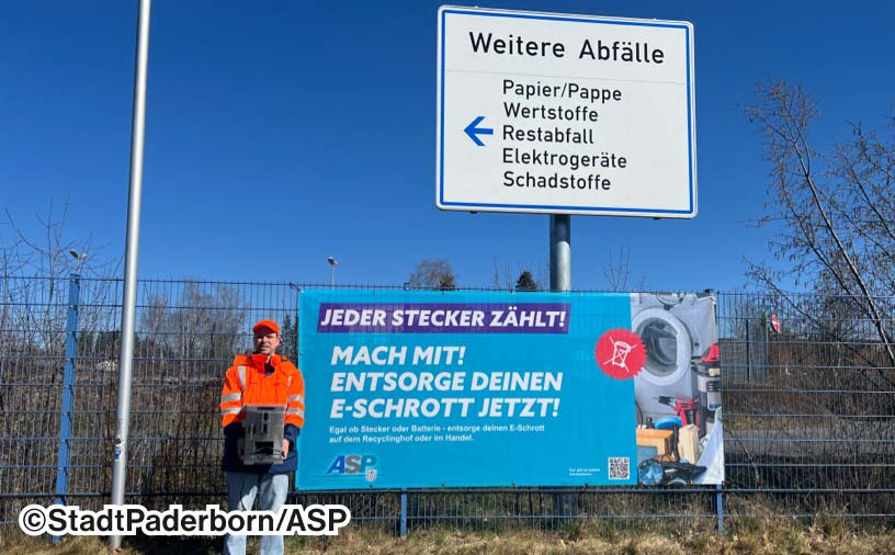 Ein Aktionsmitarbeiter, der vor einem großen Plakat der Aktion steht, mit dem Text "Jeder Stecker zählt! Mach mit! Entsorge deinen E-Schrott jetzt!"