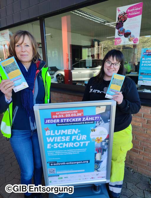 Zwei Frauen stehen vor einem Plakat der Aktion "Blumenwiese für E-Schrott"